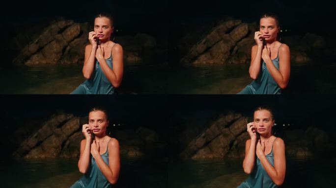 身着蓝色连衣裙的优雅女子在宁静的天然水池中放松。空灵之美，神秘气息，水润肌肤容光焕发。时尚、健康、幻