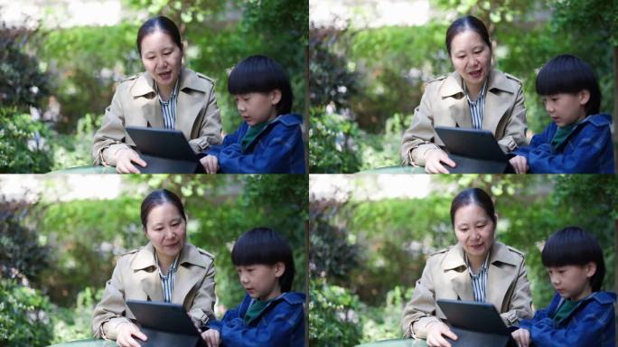 亚洲母子在院子里用平板电脑看书