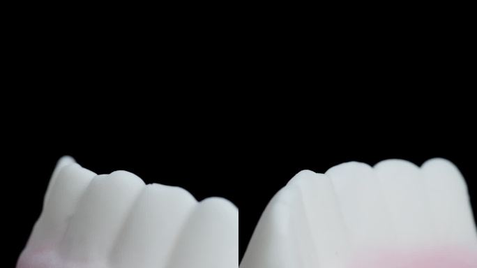 一种有粉红色牙龈的白色牙齿形状的软糖。在一个特写镜头中，它在黑色的背景上旋转，孤立的。