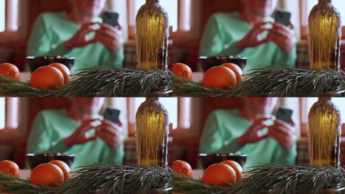 一家餐厅的木桌上放着一根圣诞树枝和鲜亮的橙子，背景是一个手里拿着手机的男人。