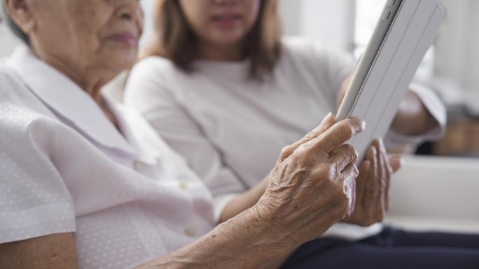 年迈的母亲带着女儿用数码平板电脑一起看难忘的照片。欢乐的家庭时刻