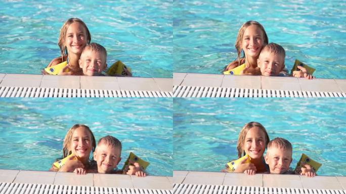 快乐的孩子们在游泳池游泳的特写。哥哥和妹妹。年轻漂亮的女孩和小男孩开怀大笑。戴着充气臂章的男孩抓住泳