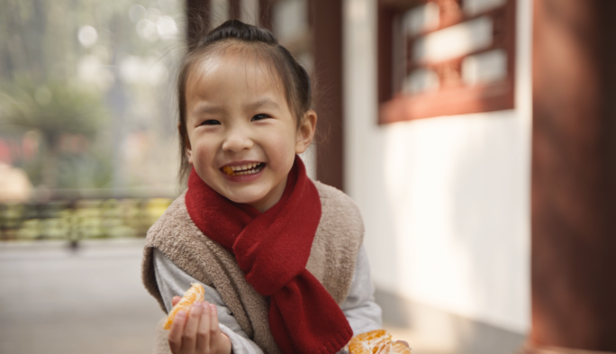 可爱小女孩围着红围巾在公园里玩耍吃橘子