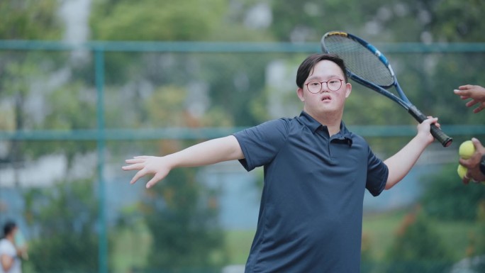 周末上午，亚裔华裔唐氏综合症男子向男教练学习打网球