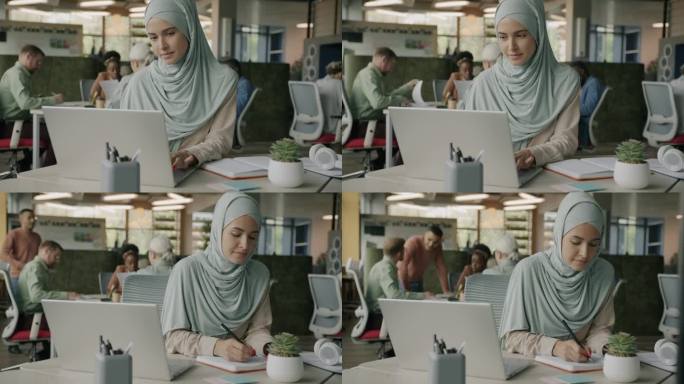 戴着头巾的穆斯林女商人在共用办公室用笔记本电脑打字和写字