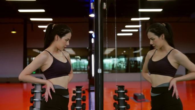 精力充沛的健身女运动员在健身房。亚洲女运动员站在窗前，看着我的身体。健身中心的美女美女和自信