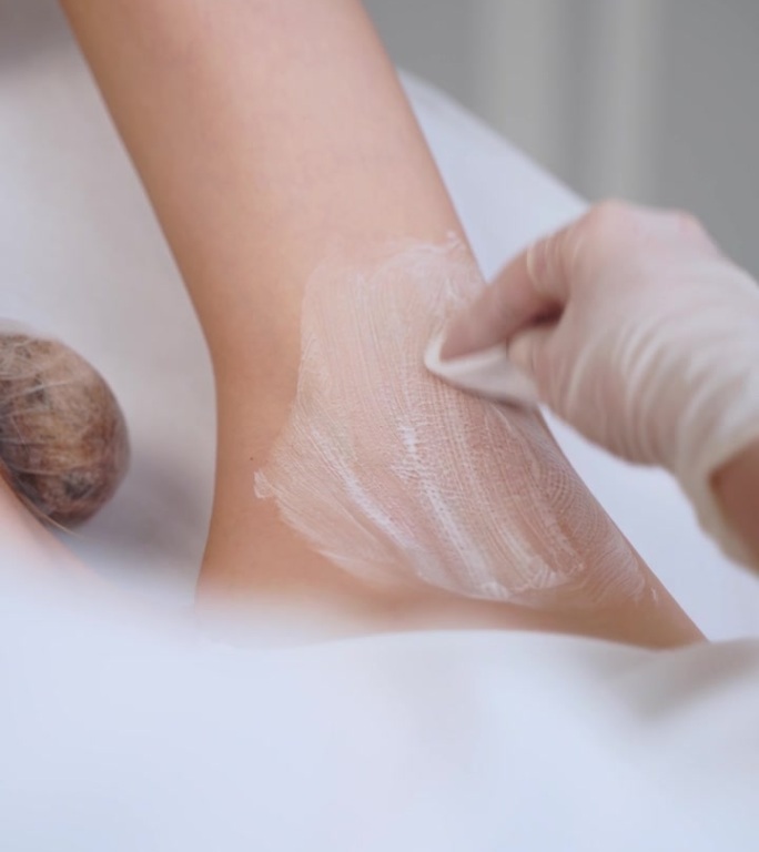 激光治疗后，手臂在诊所接受保湿霜的应用。护肤程序舒缓皮肤，促进愈合。美容师在脱毛后进行润肤护理。