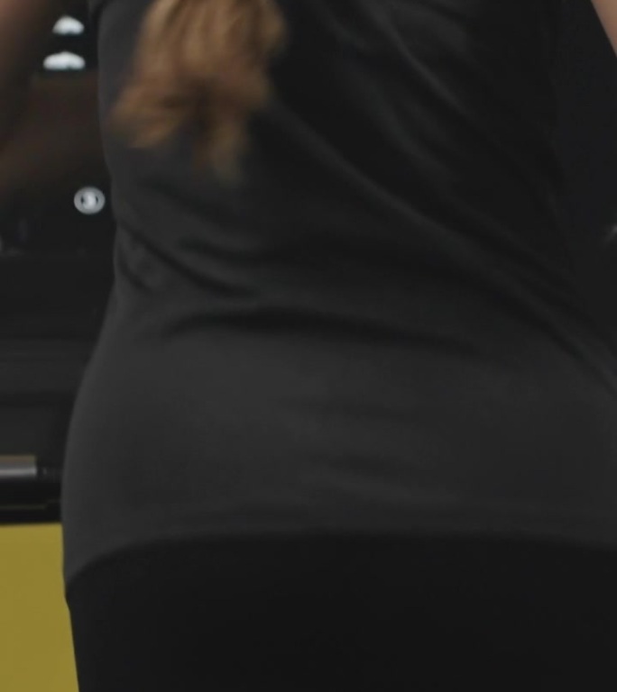 垂直视频。长头发的年轻女子在跑步机上。她背上的汗珠。有效减肥。