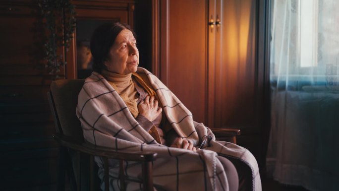 老年妇女胸痛，独自坐在扶手椅上，盖着毯子
