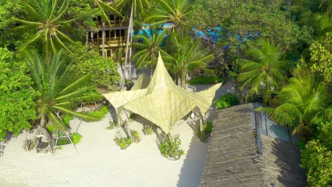 从空中俯瞰马尔代夫的白色沙滩，有大海和茅草小屋，还有郁郁葱葱的热带岛屿。
