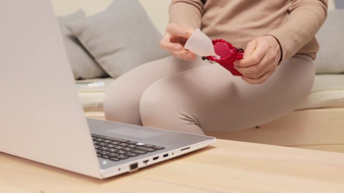 不认识的女人用笔记本电脑搜索月经杯，在互联网上使用说明，试图找到家教视频坐在家里的沙发上。