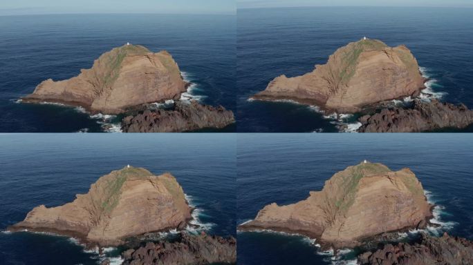 宁静的蓝绿色海洋中的巨石，上面有一座小灯塔。史诗级无人机推入倾斜向下的镜头。在葡萄牙马德拉岛的莫尼兹