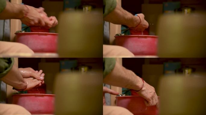 一名男性陶工在制作完陶器后在红盆里洗手的特写