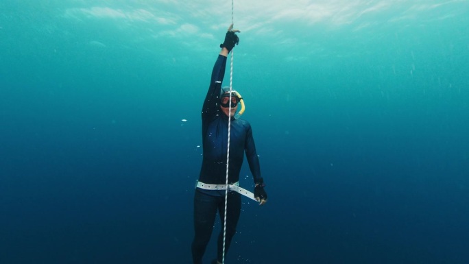 自由潜水员靠绳子练习并上升。自信的男性自由潜水员在开阔的海面上沿着绳索训练，然后从深处上升