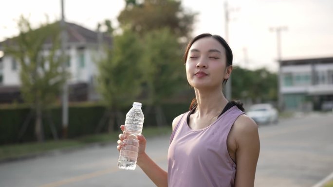 年轻的健身女性在户外公园里一边喝能量水一边做伸展运动。晚上锻炼身体，健康观念慢无影