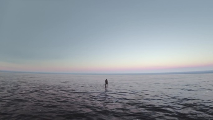 无人机拍摄的视频显示一名单身男子站在海中央望着地平线。世界末日。冥想，透视，孤独，独自面对困难的概念