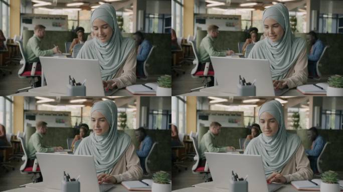 戴着头巾的穆斯林妇女用笔记本电脑在开放式办公室里享受创造性的活动