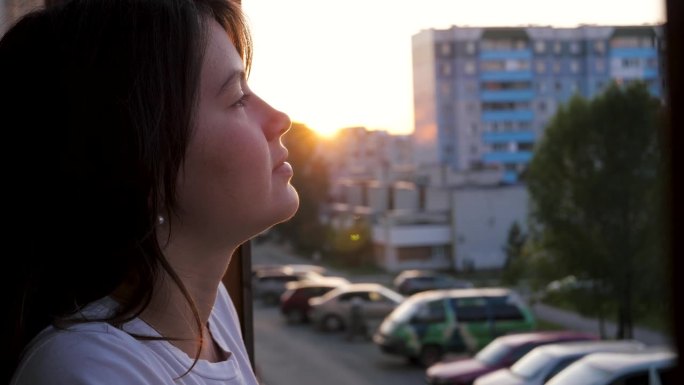 夕阳下梦幻的年轻女子走出阳台，深吸一口气