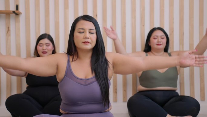 三个中等身材的亚洲女性，长着黑色的长发，穿着运动工作服，闭上眼睛，在家里做瑜伽体式，双腿交叉坐在一起