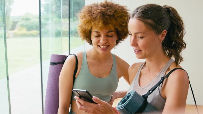 两个女性朋友穿着运动服在健身房或瑜伽馆看手机