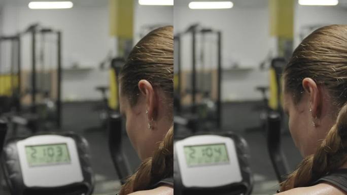 垂直视频。一个女人在健身房骑着固定自行车，踩着踏板，她的背部布满了汗珠。燃烧脂肪和活力的锻炼!