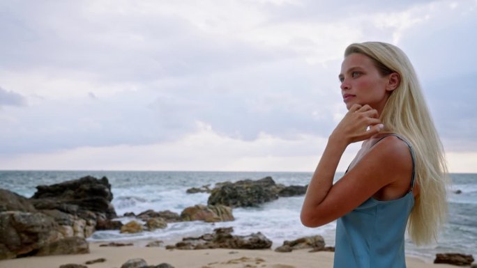 一名身着蓝色泳装的女子在海边放松，宁静的海岸。宁静的场景，女性在沙滩上看日落，海风拂面。独自旅行的人