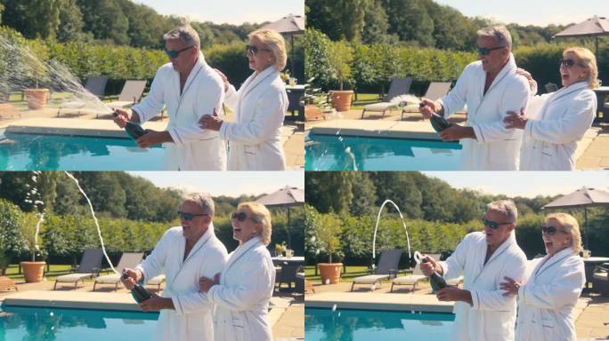 度假的老夫妇穿着长袍，在酒店游泳池边开瓶喷香槟