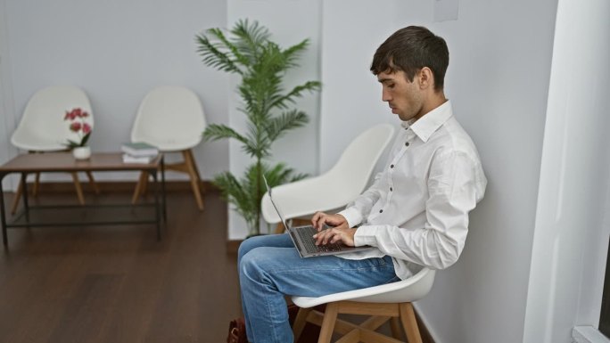 年轻英俊的西班牙人，坐在熙熙攘攘的候诊室的椅子上，用笔记本电脑全神贯注地处理严肃的事务