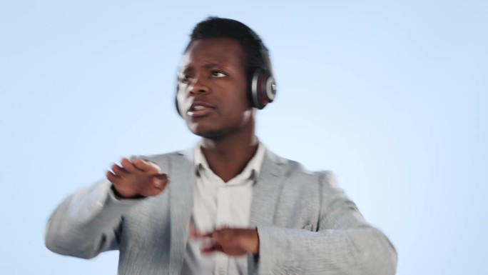 黑人，戴着耳机，在蓝色的工作室背景下随着音乐跳舞。精力充沛的非洲商人与耳机享受播客的声音，歌曲或播放