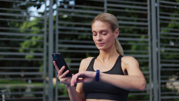 穿着运动服的年轻活跃女性在户外运动后使用健身追踪应用程序来监控她的训练进度。金发女人看了看智能手表，