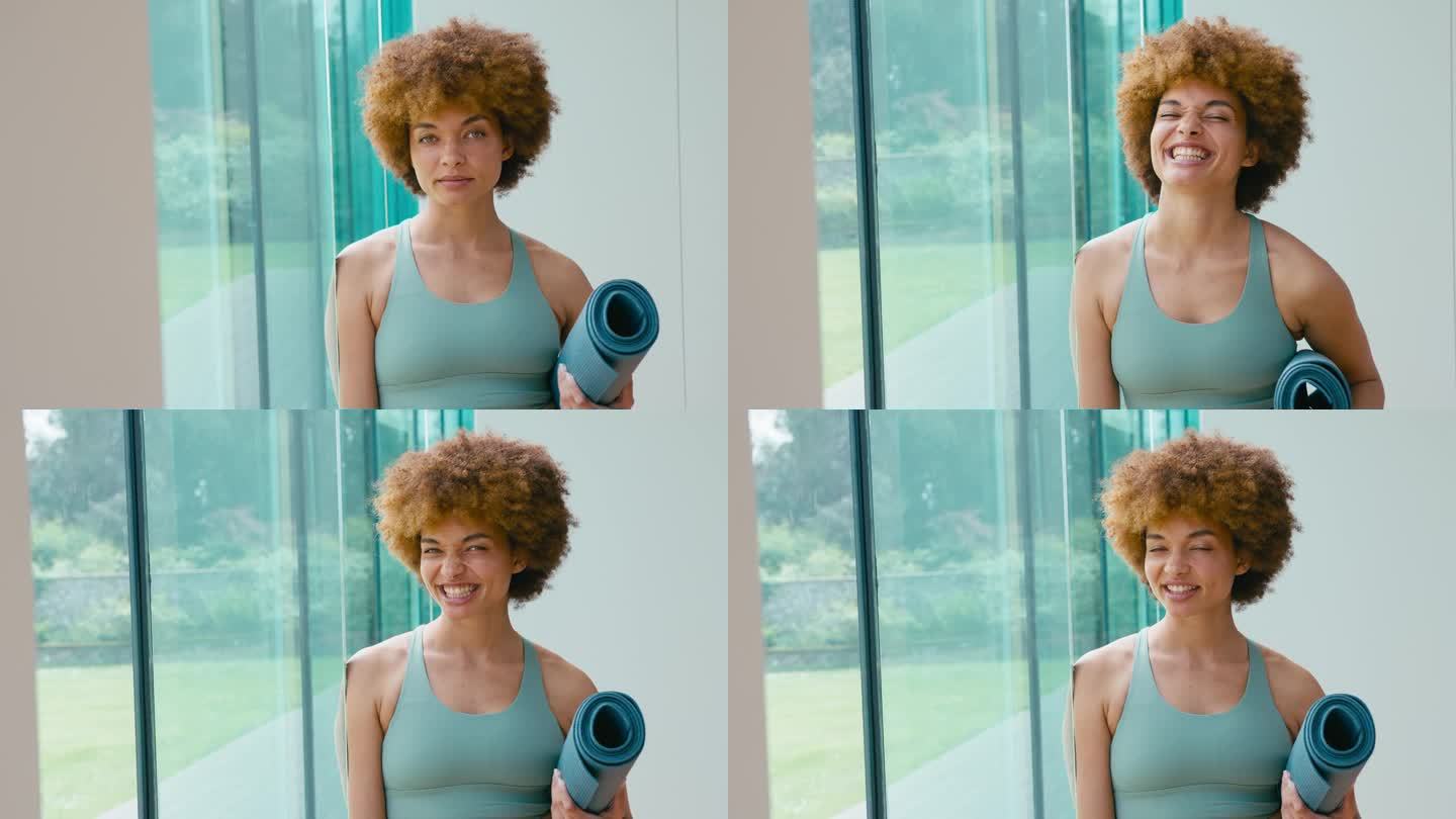 微笑的女人在健身房或瑜伽馆穿着运动服拿着运动垫的肖像