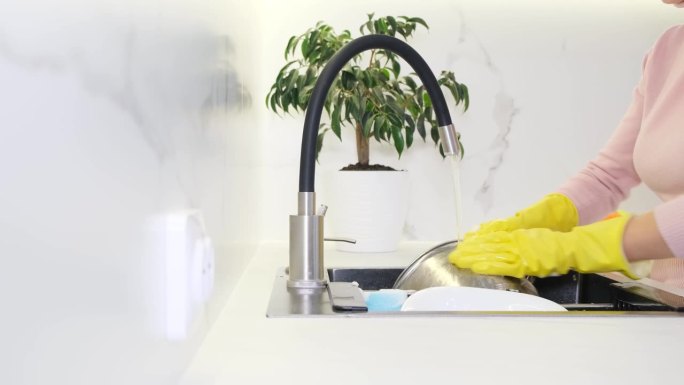 一个戴手套的女人在厨房里用水和脱脂剂洗碗盘。