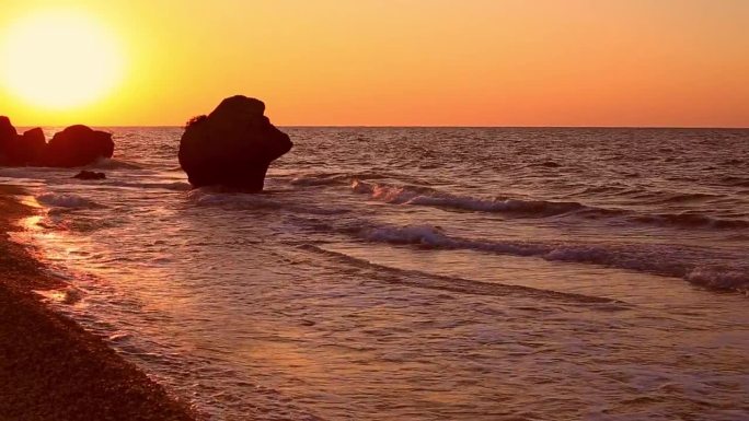 海边的日落。在夕阳的照耀下，一股波浪卷向岸边，一块巨石矗立在岸边