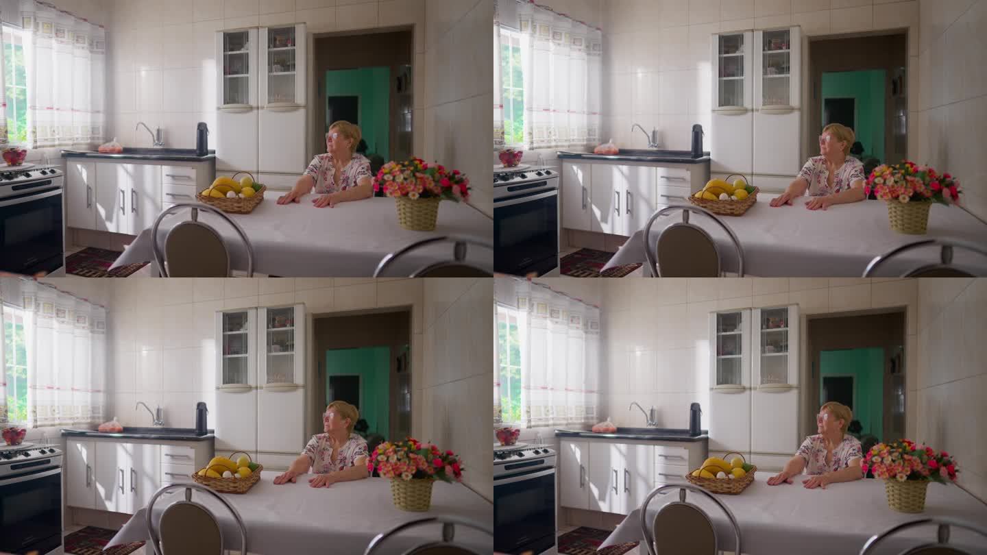 沉思的老年妇女坐在厨房的桌子上看着窗外。真诚周到地表达了现实生活中老年人的居家生活方式