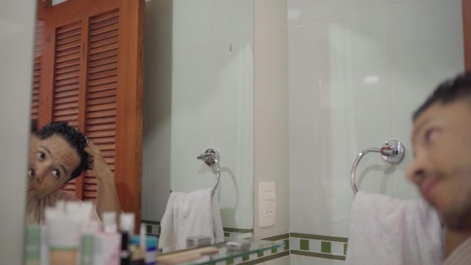 一个年轻人在淋浴后对着浴室的镜子做发型