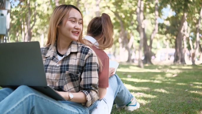 两名女学生坐在大学校园的草地上一起工作和学习考试