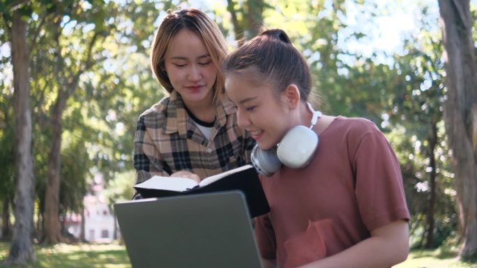 两名女学生坐在大学校园的草地上一起工作和学习考试