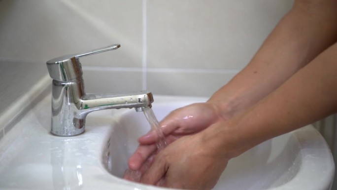 男子的手打开水龙头，在浴室洗脸盆洗手。清洁健康的理念。