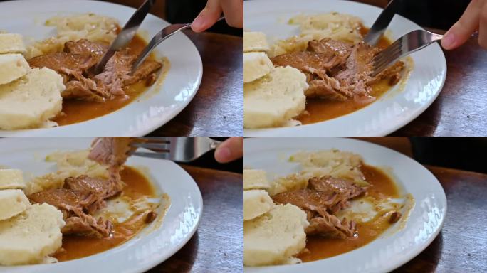 2023年8月4日，捷克共和国布拉格。慢镜头特写的典型菜肴之一:酸菜炖猪肉和蘸面包。手拿刀叉切一块肉