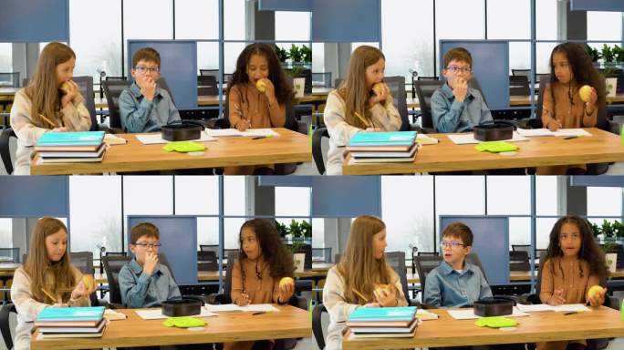 不同的学生在教室里一起坐在桌子上吃苹果聊天