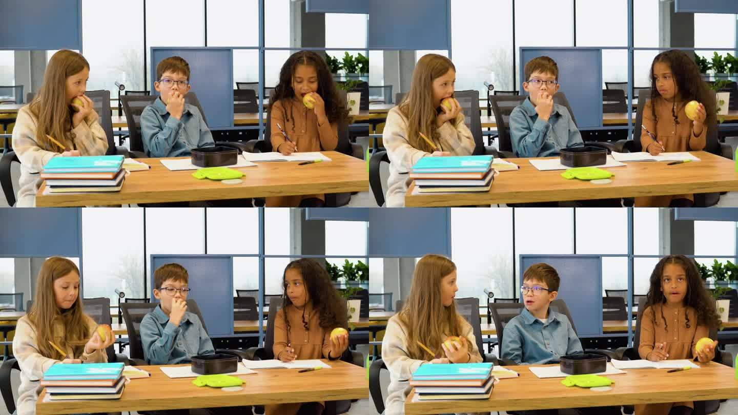 不同的学生在教室里一起坐在桌子上吃苹果聊天
