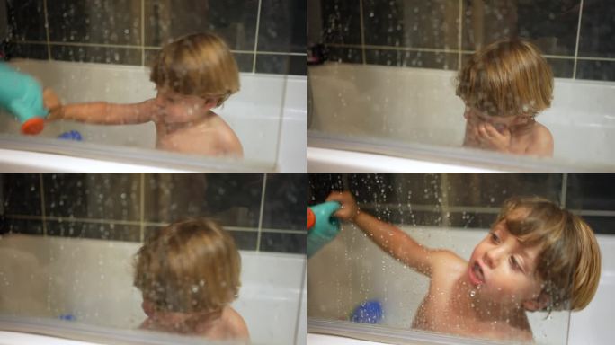 一个小男孩在浴缸里玩耍，透过玻璃可以看到孩子洗澡时的样子。孩子自己玩得开心