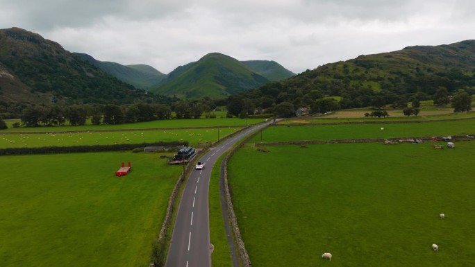 白色的电动汽车行驶在乡村公路上，穿过绿色的草地，背景是史诗般的山脉。