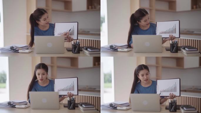 一名亚洲女性用笔记本电脑在互联网上展示和解释盈亏图表。她坐在家中现代简约风格厨房的餐桌旁。