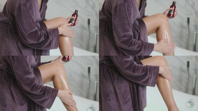 在家里的浴室里，一位穿着浴袍的女士把腿放在浴缸里，正在给腿涂油。腿的特写镜头。