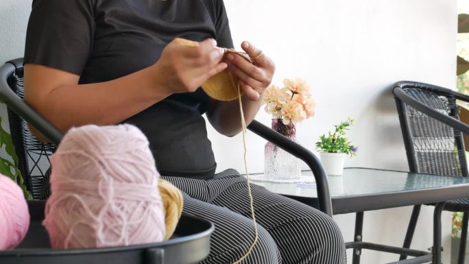 亚洲妇女拿着钩针，享受编织，坐在花园椅子上。女性手工编织手巾，女士手工工艺爱好概念，4k。