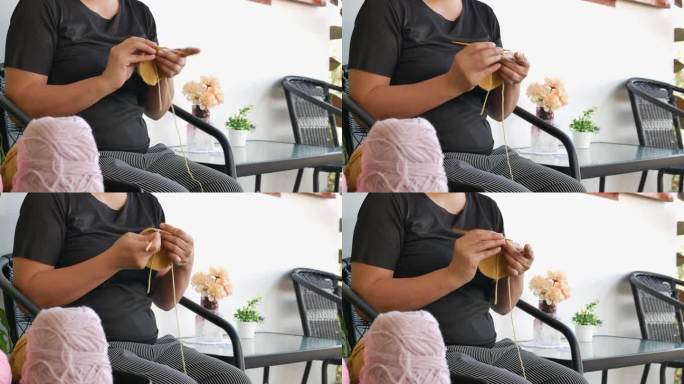 亚洲妇女拿着钩针，享受编织，坐在花园椅子上。女性手工编织手巾，女士手工工艺爱好概念，4k。