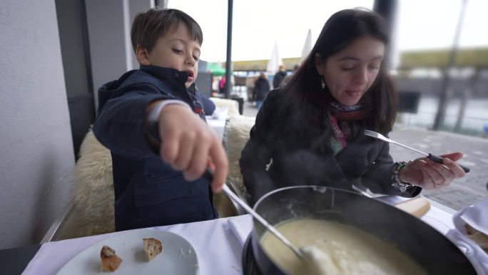 母亲和儿子在户外餐厅吃火锅，人们在瑞士享受传统的欧洲食物，冬天的热面包和奶酪