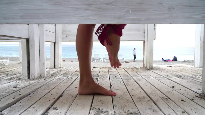 女人在海滩上的更衣间里，在日落的海边。女孩换了衣服，抛出了一件泳衣，然后穿着一件粉红色的裙子离开了更