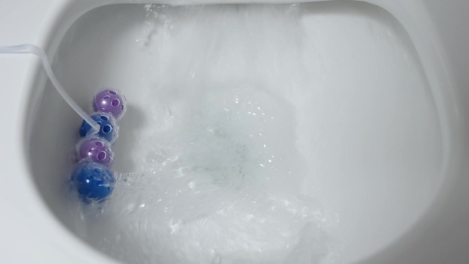 马桶冲水，马桶清新块与蓝色和紫色球接近。厕所里的香球